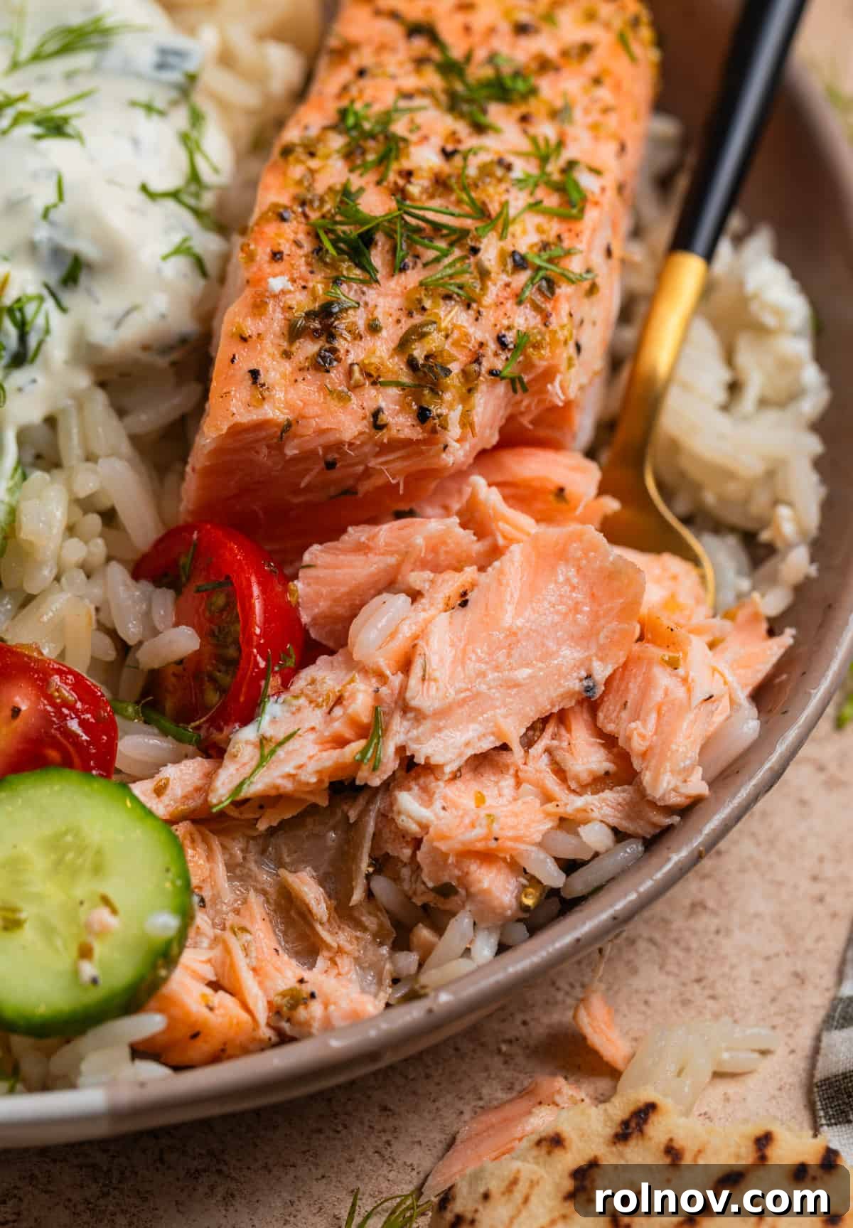 Zesty Greek Salmon & Herb Rice Bowls 9 Salmon in dish with rice and veggies with fork and part of the salmon flaked.