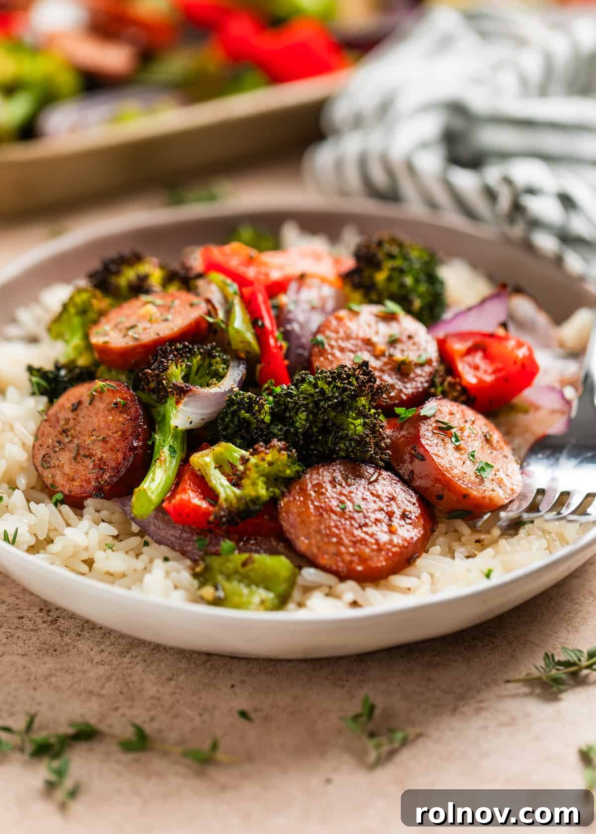 Roasted Sausage & Veggie Sheet Pan Supper 3 Kielbasa pork sausage and veggies over rice on plate with fork.