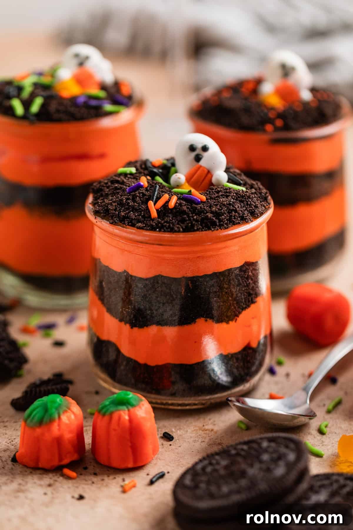 Halloween Oreo Graveyard Cake 7 Orange and black layered pudding and crushed Oreos in glass jars with Halloween themed sprinkles and candy.