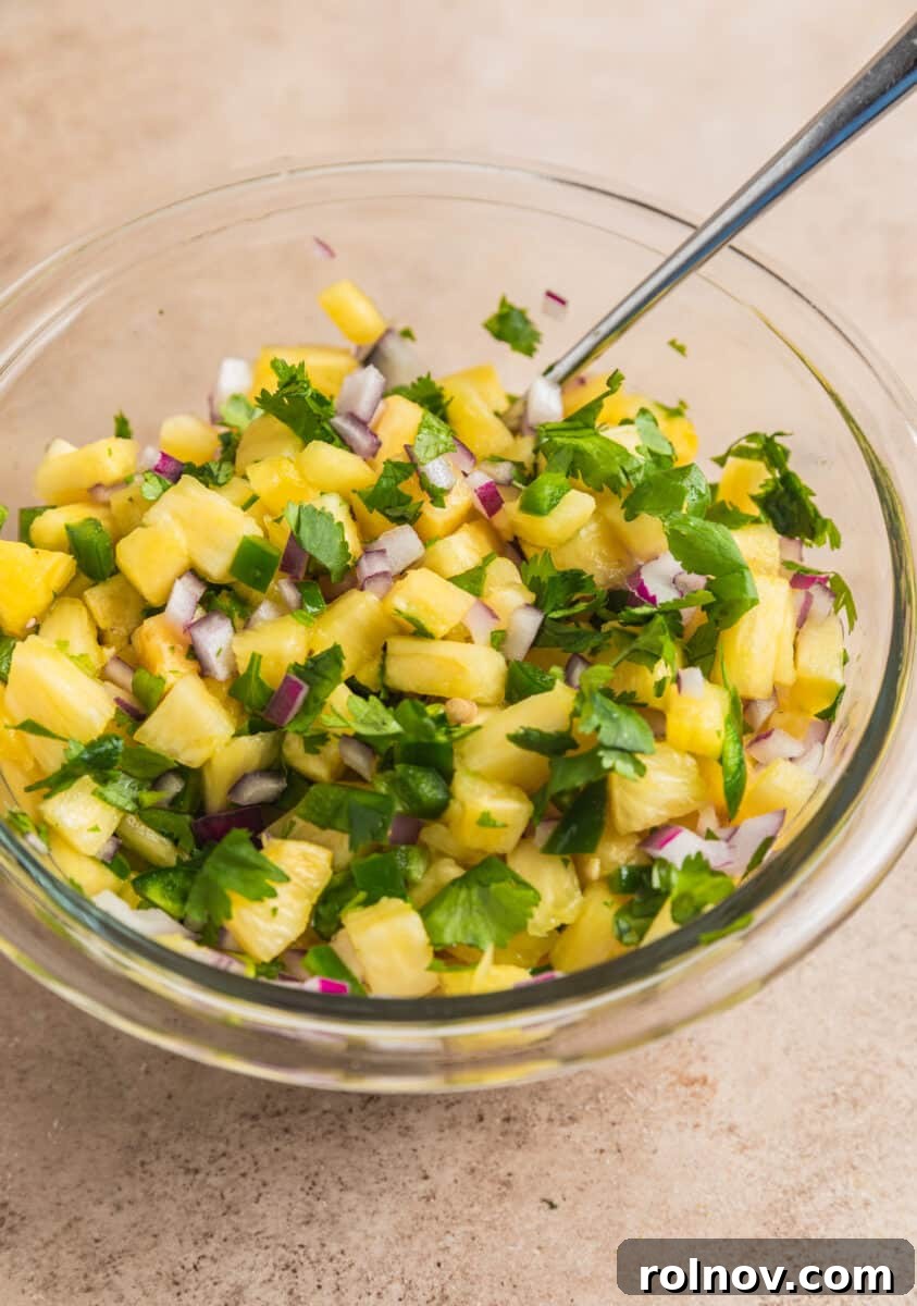 Zesty Pork Tacos with Fresh Pineapple Salsa 6 Spoon scooping into glass bowl with pineapple salsa.