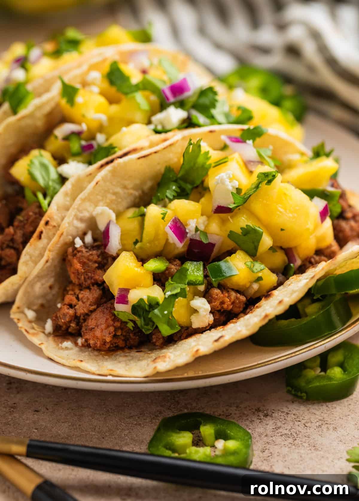 Zesty Pork Tacos with Fresh Pineapple Salsa 9 Pork tacos topped with pineapple salsa on plate with sliced jalapeños nearby.