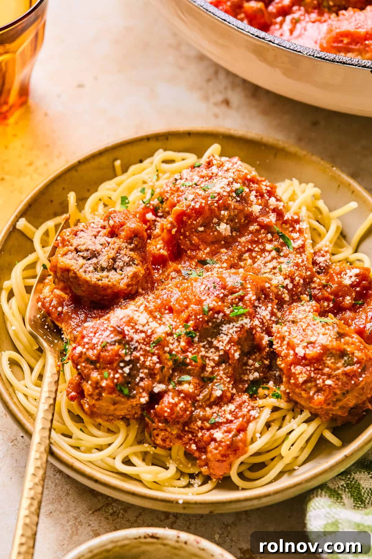 Spaghetti and meatballs in dish with fork, garnished with fresh basil.