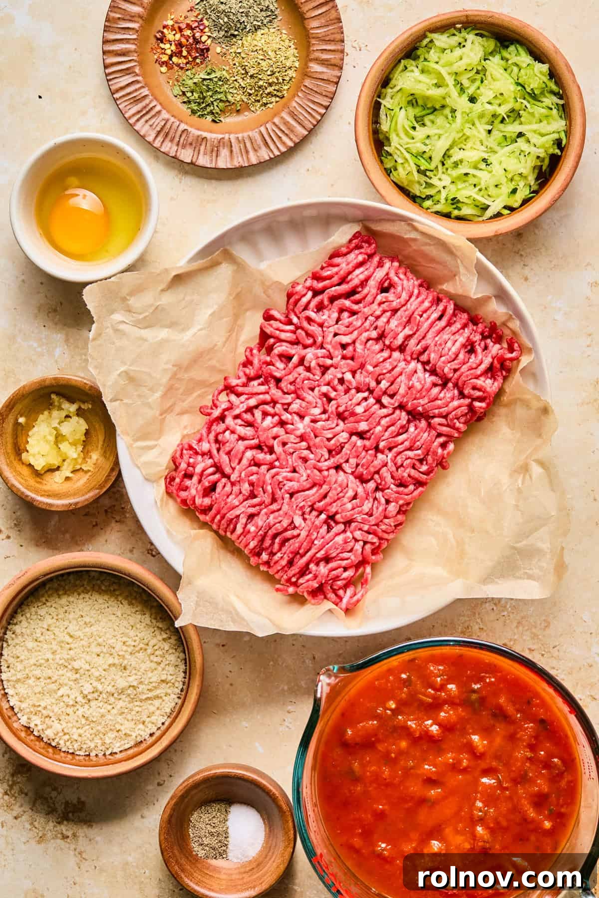 Ground beef, marinara sauce, shredded zucchini, and other fresh ingredients laid out on a kitchen surface before mixing.