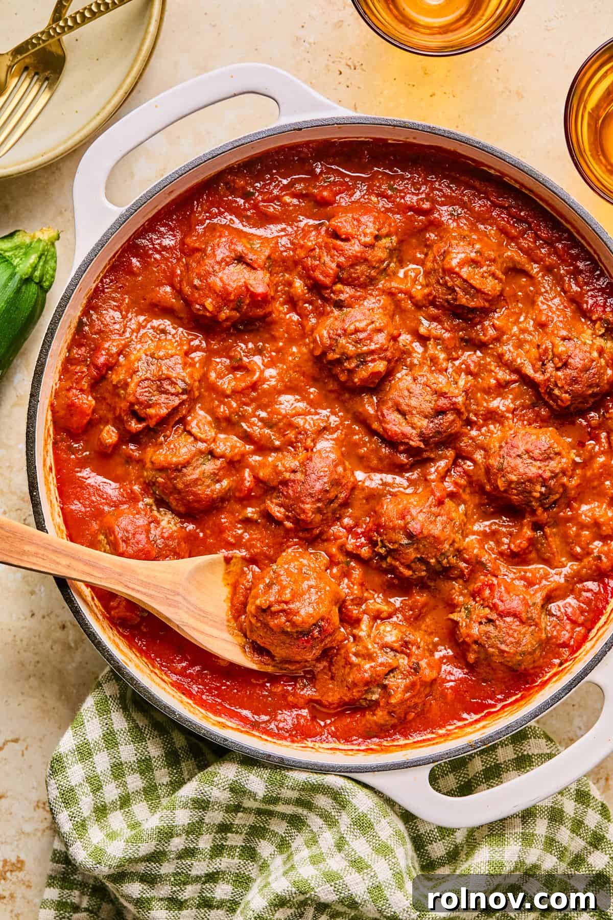 Beef and zucchini meatballs simmering in a pot with rich marinara sauce, with a wooden spoon resting inside.
