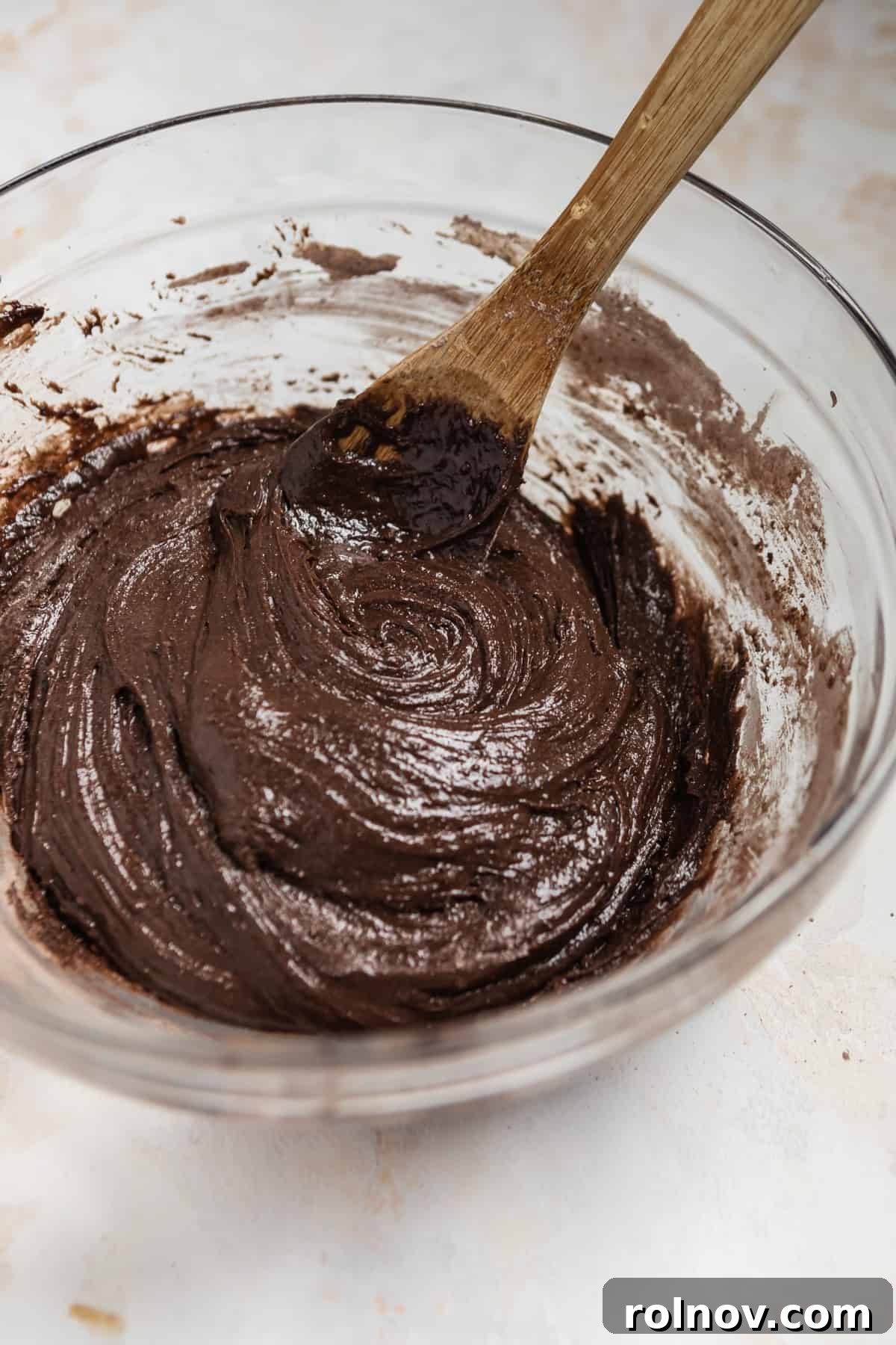 Effortless Chocolate Cake Mix Treats 5 A glass mixing bowl filled with rich, sticky chocolate cookie dough, accompanied by a wooden spoon, ready for chilling.