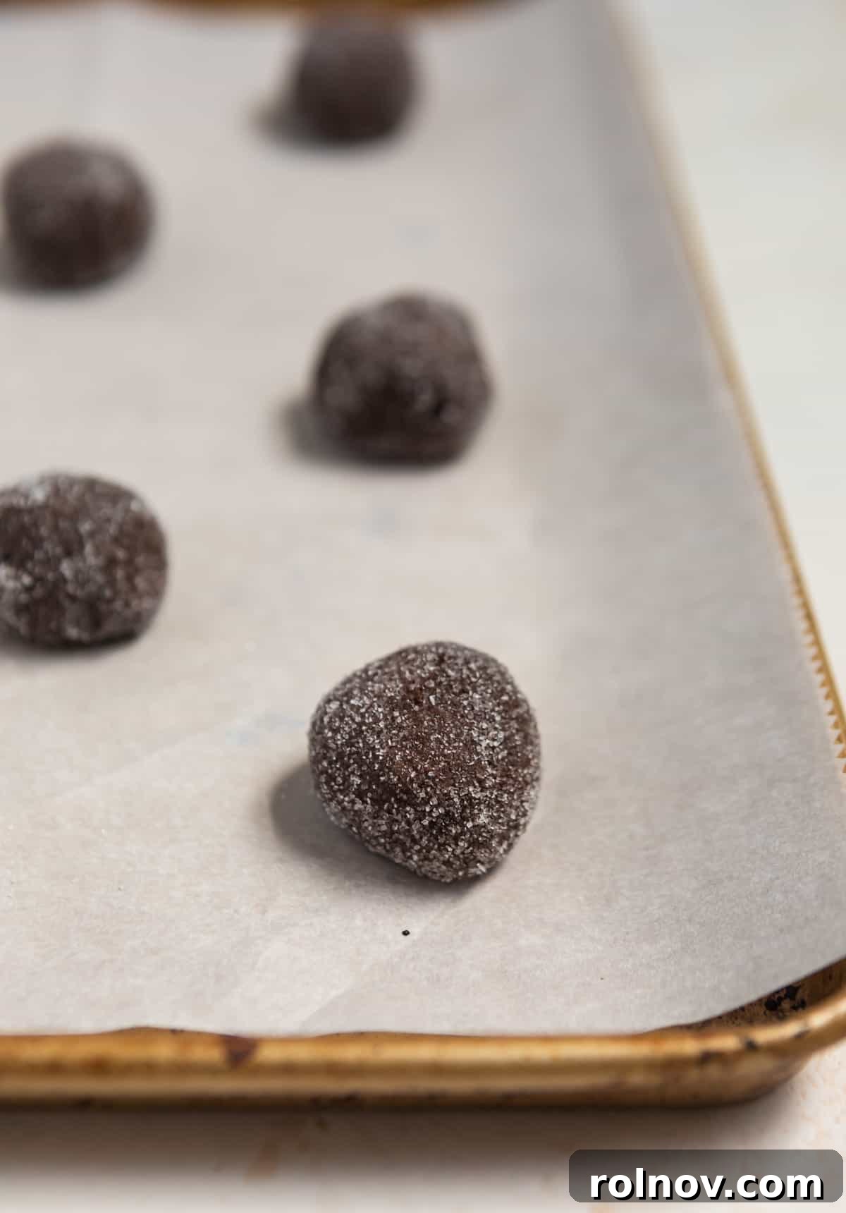 Effortless Chocolate Cake Mix Treats 6 Neatly arranged chocolate cookie dough balls, coated in sugar, patiently waiting on a parchment-lined baking sheet before entering the oven.