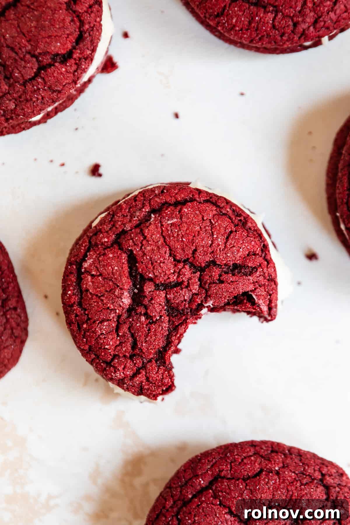 Scarlet Velvet Cake Mix Cookies with Tangy Cream Cheese Frosting 7 Overhead view of a red velvet sandwich cookie with a bite taken out, showcasing the creamy filling, on a rustic surface.