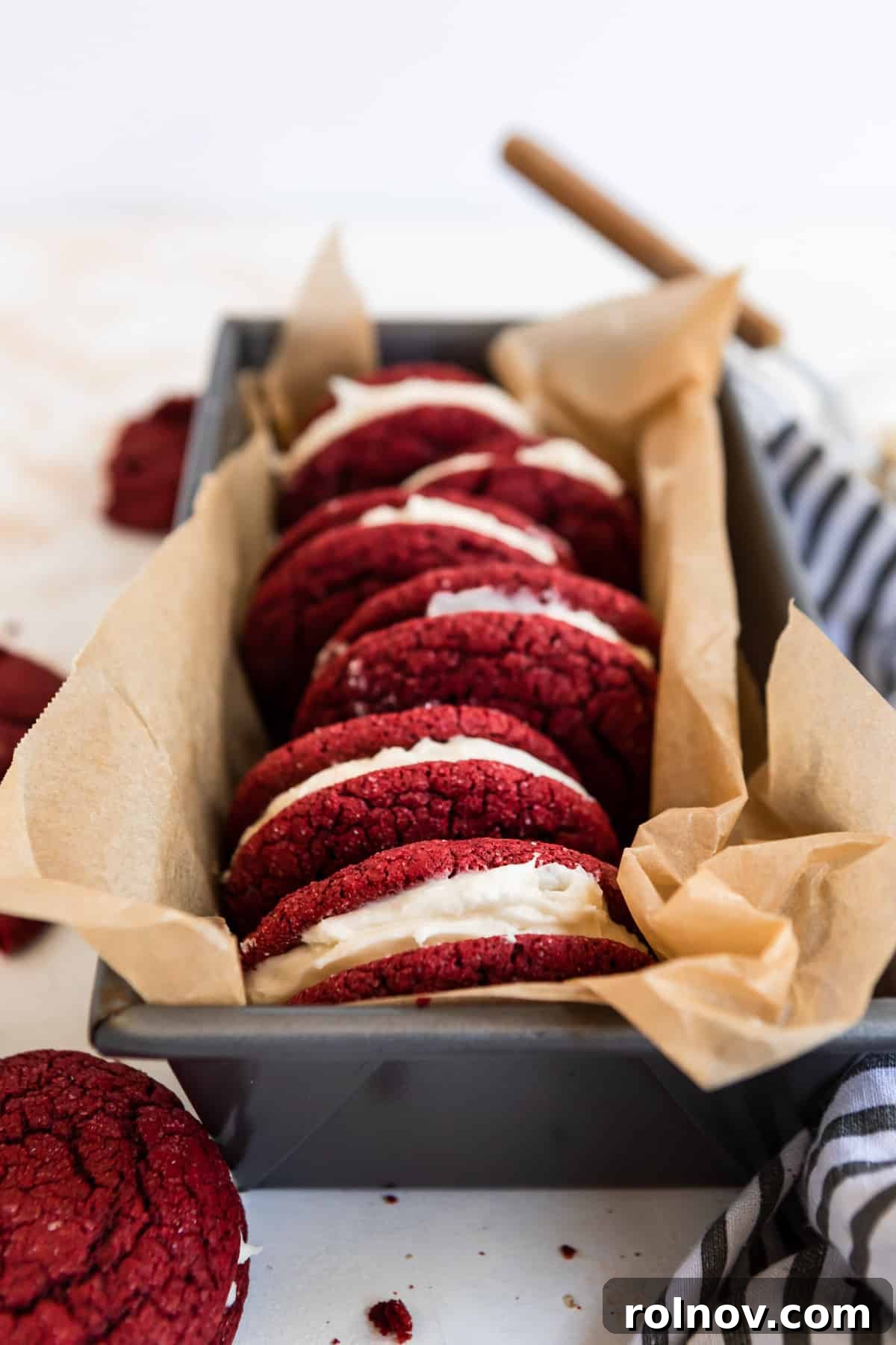Scarlet Velvet Cake Mix Cookies with Tangy Cream Cheese Frosting 8 Red velvet cake mix sandwich cookies arranged neatly in a bread pan lined with parchment paper, ready for storage or serving.