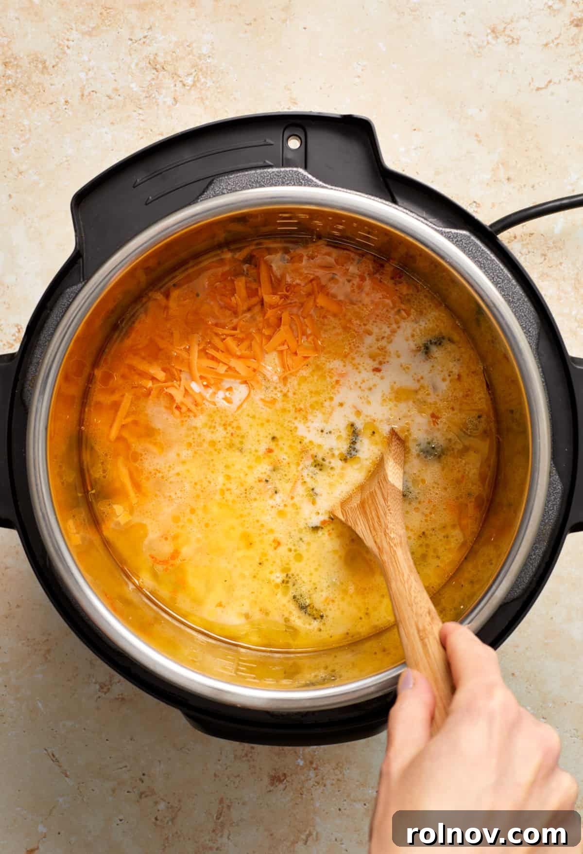 Creamy Instant Pot Broccoli Cheddar Soup 7 Creamy half and half and shredded cheddar cheese are being added to the hot soup in the Instant Pot, stirred gently with a wooden spoon to incorporate and melt.