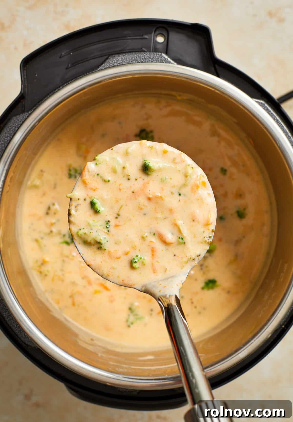 Creamy Instant Pot Broccoli Cheddar Soup 10 A ladle full of rich, creamy broccoli cheddar soup is held above the Instant Pot, showcasing the soup's perfect texture and inviting warmth.