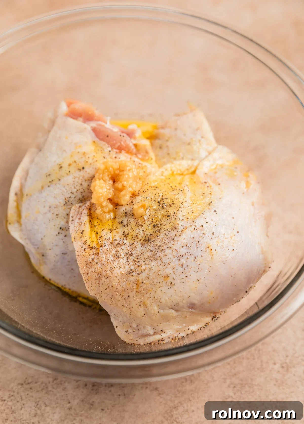 Crispy Parmesan Air Fryer Chicken Thighs 4 Raw chicken thighs in a clear glass bowl, glistening with olive oil, minced garlic, salt, and pepper, ready for the next step of preparation.