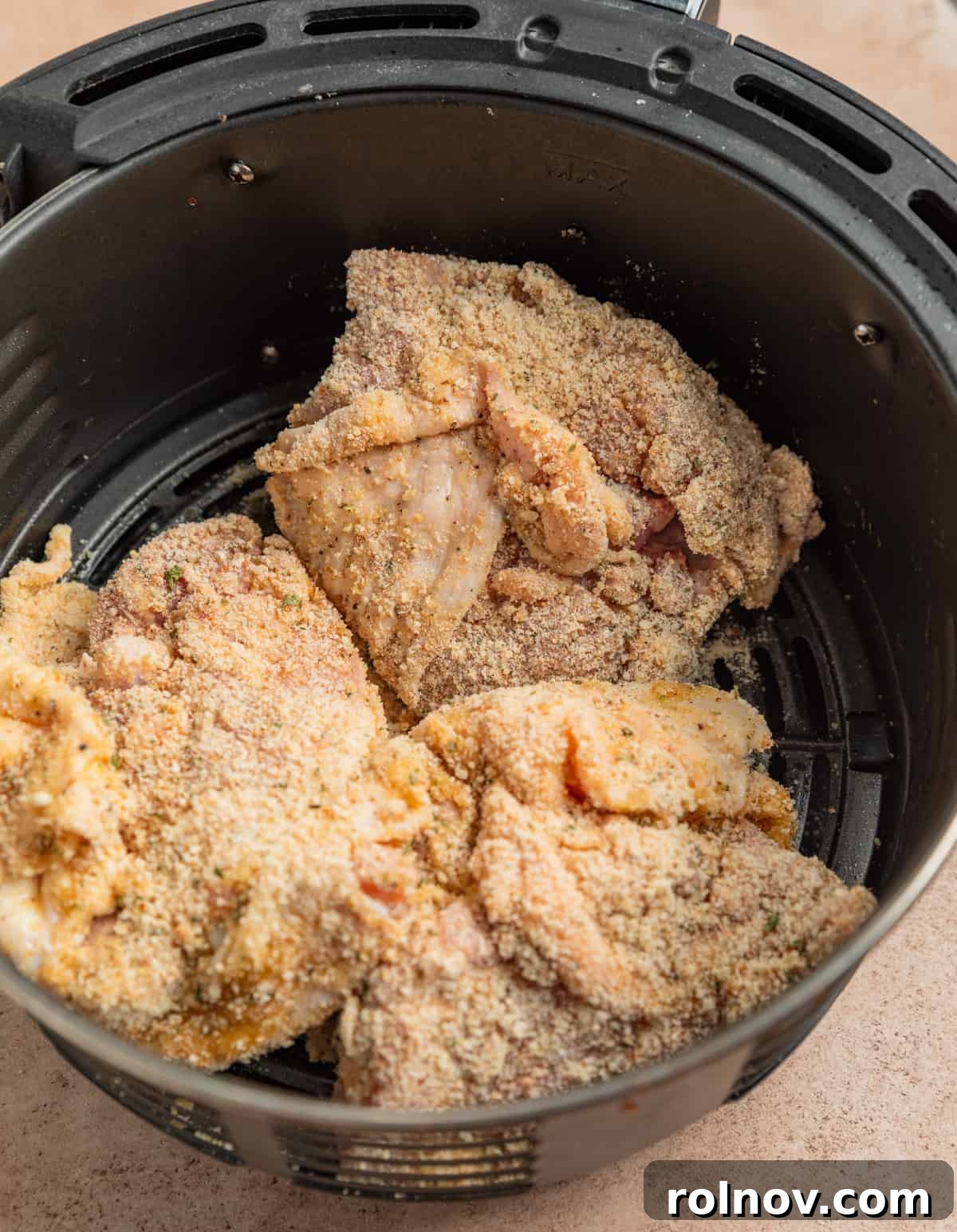 Crispy Parmesan Air Fryer Chicken Thighs 6 An air fryer basket filled with breaded chicken thighs, carefully arranged with space between each piece for optimal air circulation during cooking.