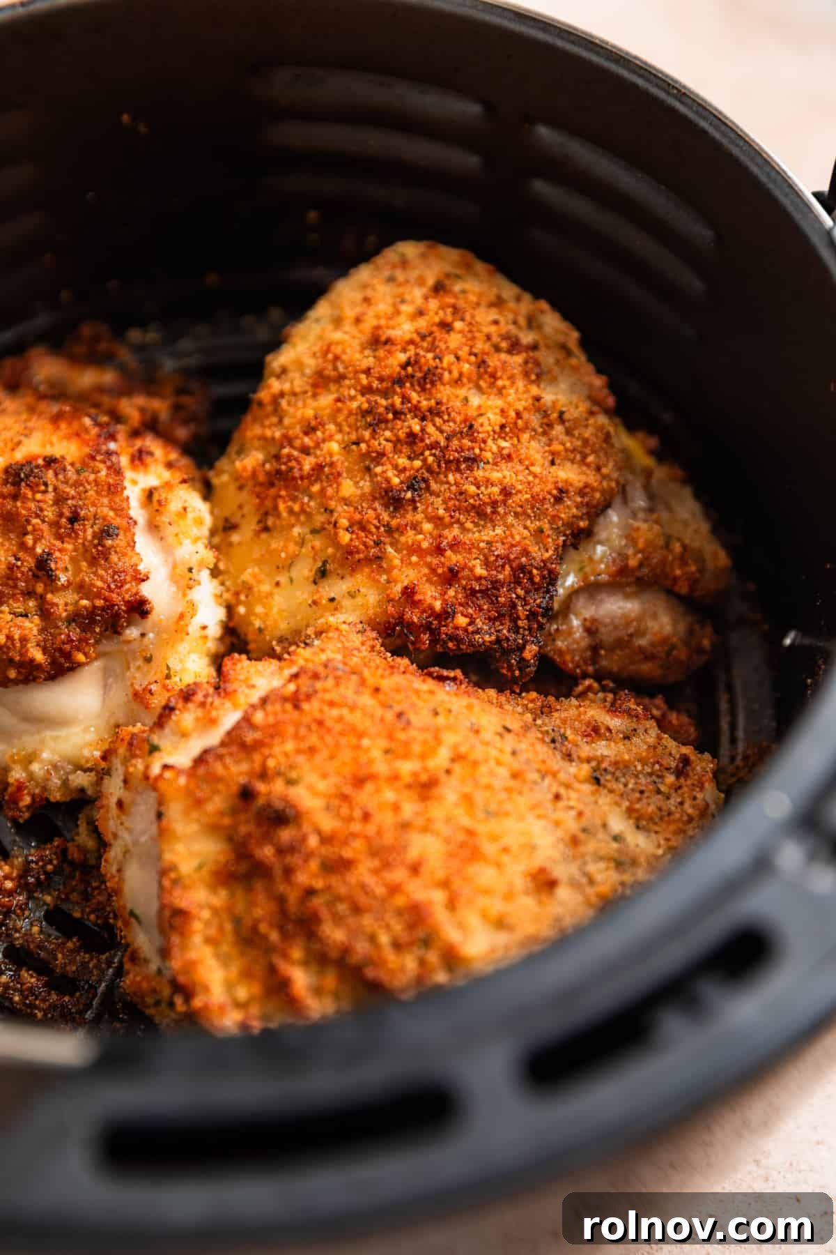 Crispy Parmesan Air Fryer Chicken Thighs 7 An air fryer basket showcasing beautifully crispy, golden-brown breaded parmesan chicken thighs, freshly cooked and ready to be served.