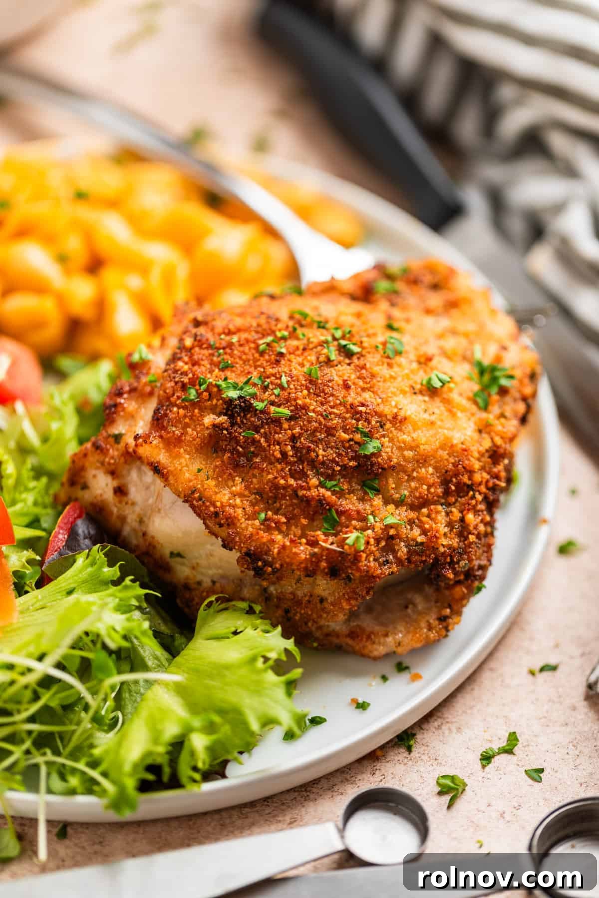 Crispy Parmesan Air Fryer Chicken Thighs 9 A beautifully plated white dish featuring a crispy breaded chicken thigh, a side portion of creamy macaroni and cheese, and a fresh green salad.