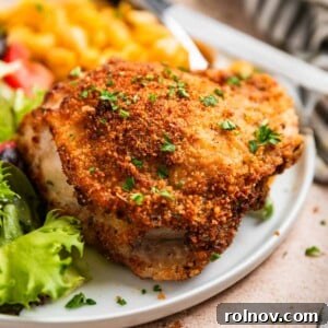 Crispy breaded air fryer parmesan chicken thigh on white plate topped with parsley.
