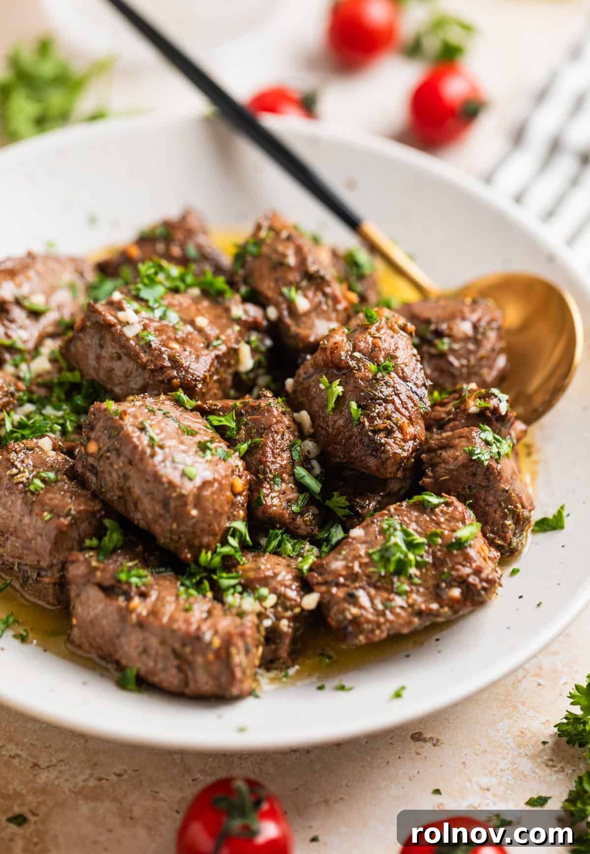 Succulent Air Fryer Steak Bites 2 White serving dish with air fryer steak bites in lemon garlic butter sauce topped with chopped parsley.