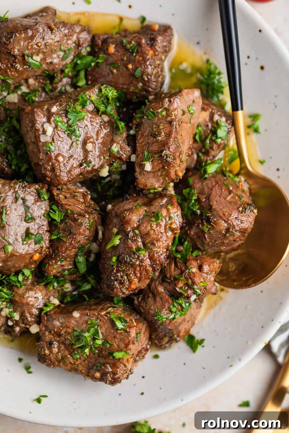 Succulent Air Fryer Steak Bites 11 Overhead view of white dish with air fryer steak bites in lemon garlic butter sauce with fresh parsley over top.