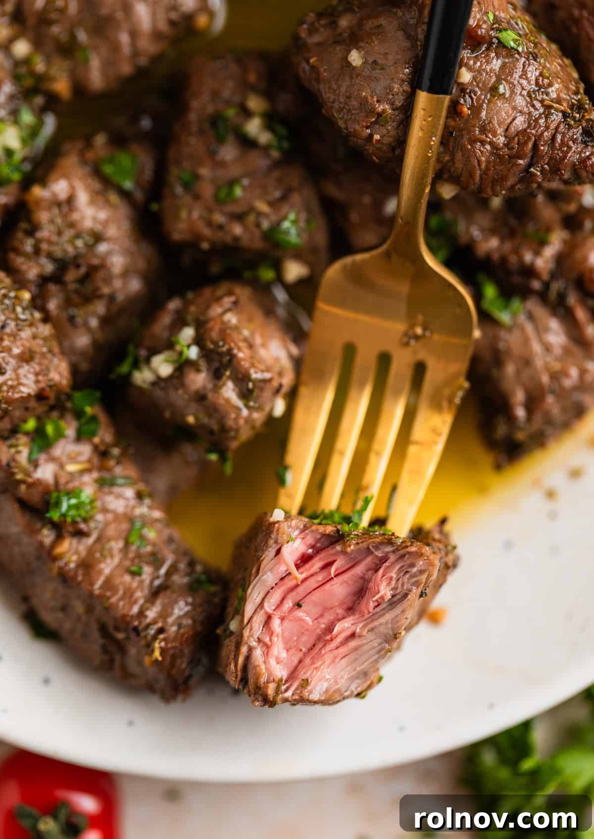 Succulent Air Fryer Steak Bites 3 Piece of steak on fork with other steak chunks to show the inside of the meat.