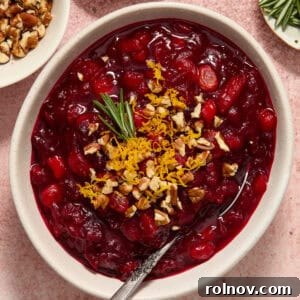 Bowl of apple cranberry chutney with orange zest, pecans and rosemary on top.