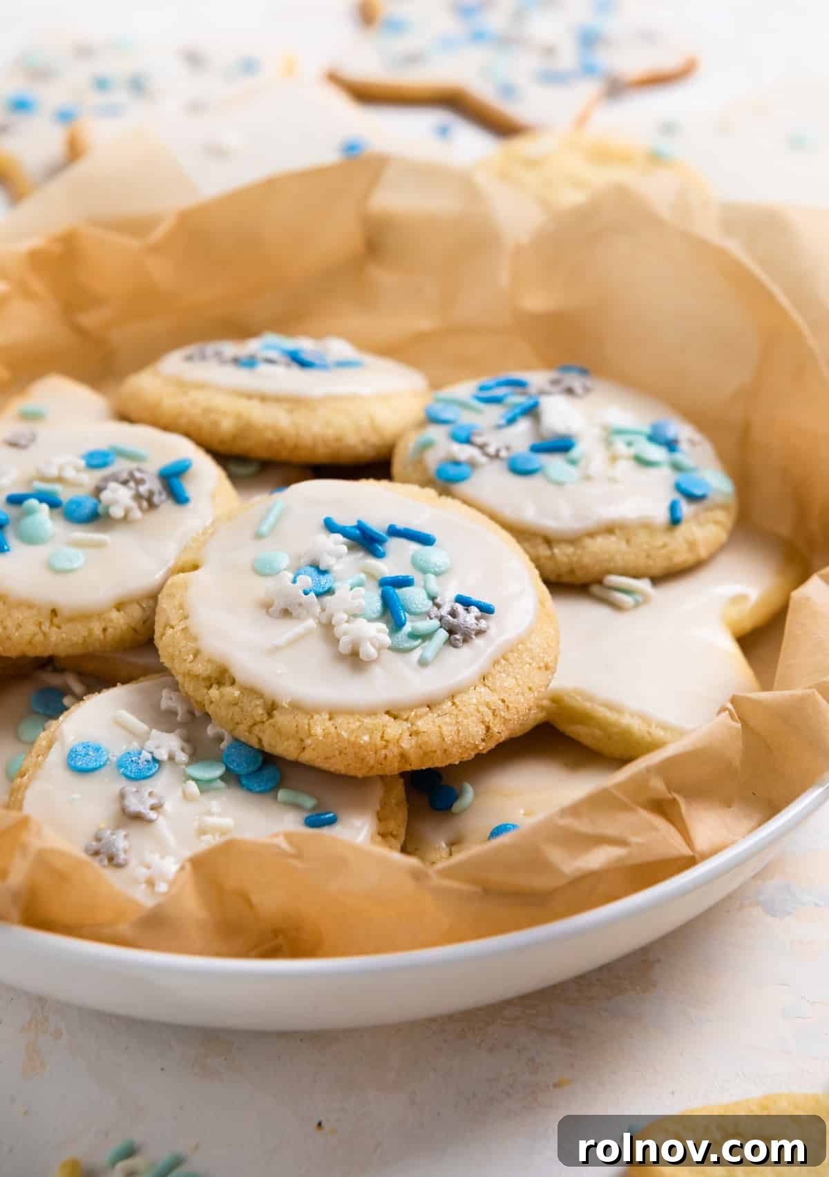 A pristine white plate showcases a selection of beautifully iced egg-free sugar cookies, each topped with a scattering of colorful sprinkles.