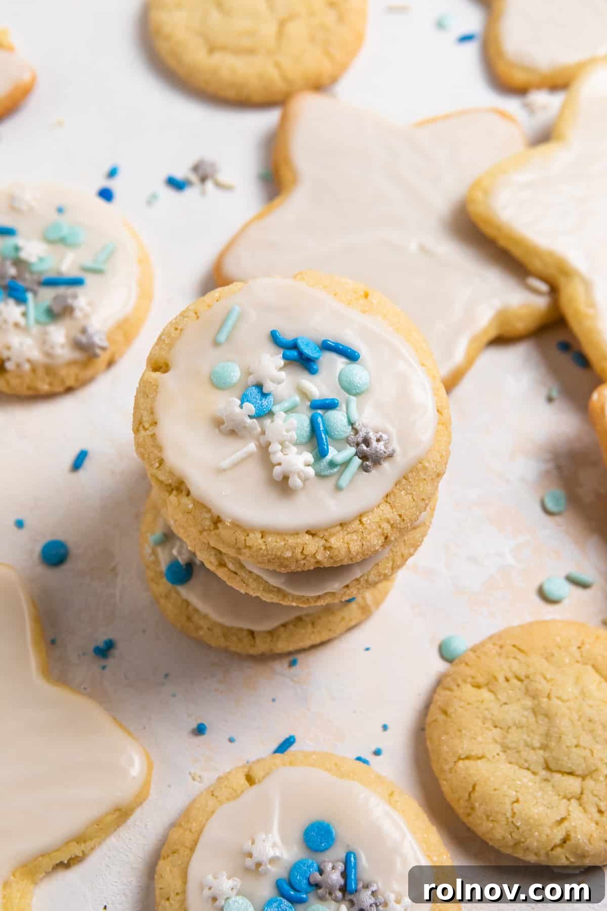 A charming stack of eggless sugar cookies, each perfectly iced with white frosting and adorned with cheerful blue sprinkles.