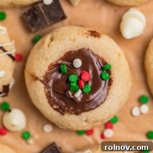 Nutella thumbprint cookies on parchment topped with red, white and green sprinkles.