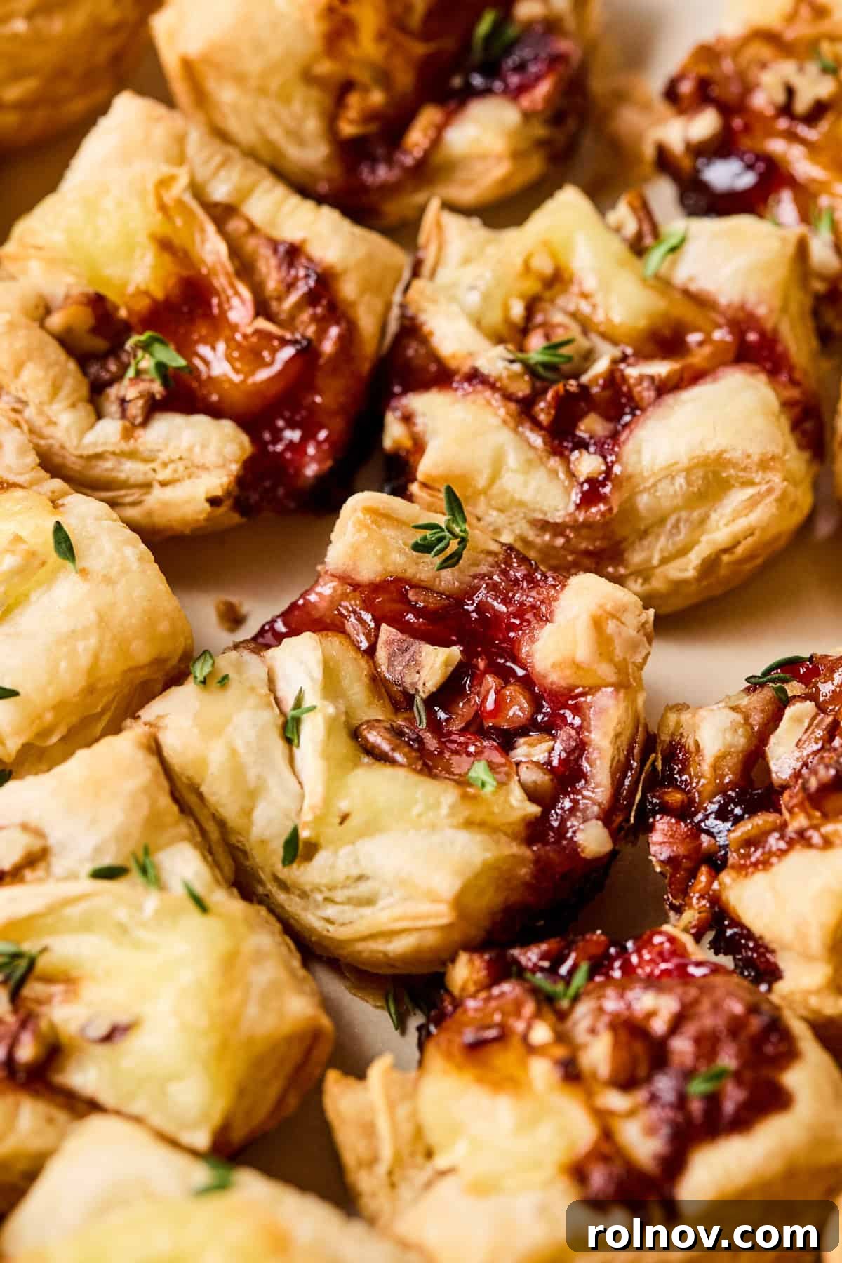 Golden Brie Pastry Parcels 2 Golden brown puff pastry brie bites on a serving plate, garnished with fresh thyme leaves.