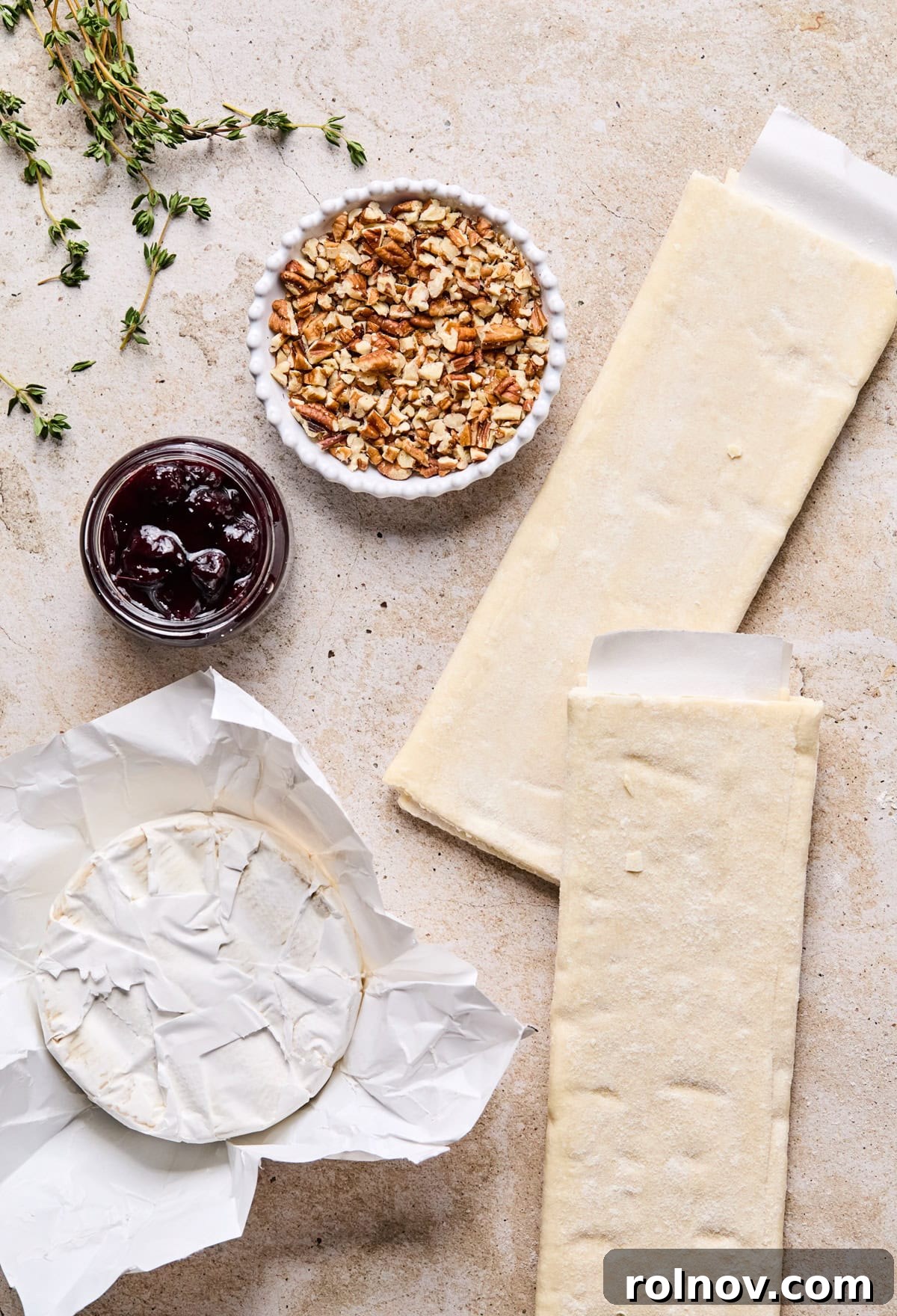 Golden Brie Pastry Parcels 3 Arrangement of puff pastry sheets, a wheel of brie cheese, jars of preserves, and fresh thyme on a wooden surface, ready for preparation.