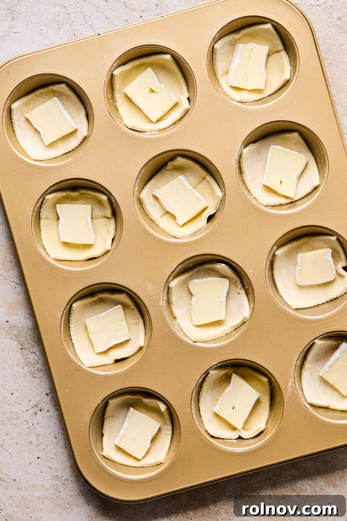 Golden Brie Pastry Parcels 5 Muffin tin with puff pastry squares pressed into cavities, each filled with a piece of brie cheese.