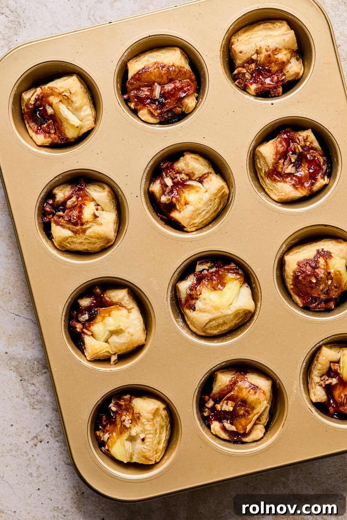 Golden Brie Pastry Parcels 7 Baked puff pastry brie bites cooling in a muffin tin, golden brown and puffed up.