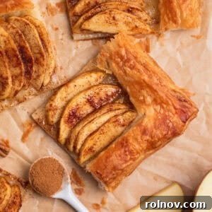 Overhead view of apple tarts on parchment with a spoonful of cinnamon beside.