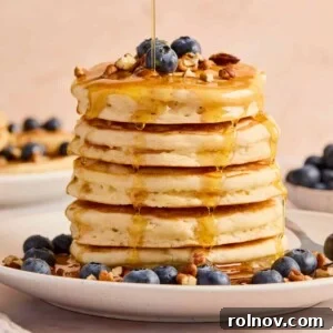 Stack of super fluffy pancakes on a plate with blueberries, pecans, and maple syrup.