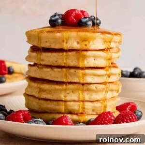 Stack of pancakes topped with berries and maple syrup being poured from above.