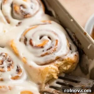 Iced buttermilk cinnamon rolls in a baking pan with a serving spatula.