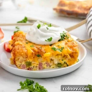Breakfast casserole with tater tots on a white plate with parsley and sour cream.