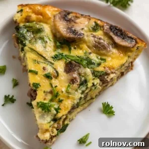 Crustless mushroom quiche with beef, swiss, and spinach on a white plate, topped with chopped parsley and chives.