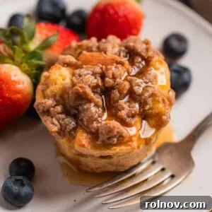 Baked French toast muffin with streusel topping on a plate with maple syrup poured over top.