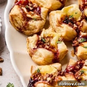 Golden puff pastry brie bites on a elegant serving platter, topped with a hint of jam, perfect for a sophisticated party appetizer.