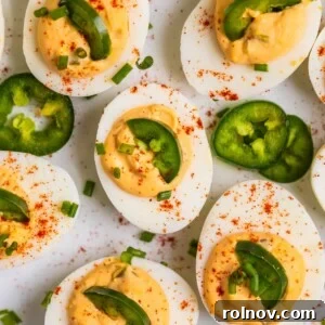 A plate of perfectly prepared spicy deviled eggs, garnished with chopped chives, pickled jalapeños, and a dusting of paprika.