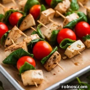 Marinated tomato, basil, and mozzarella skewers neatly arranged on a parchment-lined pan, glistening with marinade.