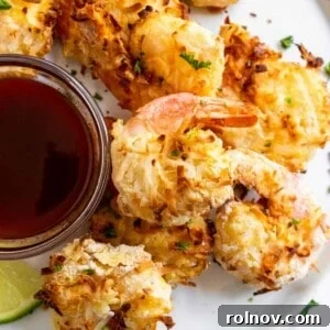 Crispy and golden air fryer coconut shrimp artfully arranged on a white plate, served with a vibrant honey sriracha dipping sauce.