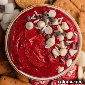 Overhead view of a rich red velvet cheesecake dip in a festive bowl, generously topped with colorful sprinkles and chocolate chips.