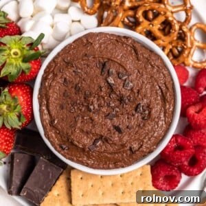 A white bowl brimming with rich chocolate brownie batter hummus, artfully surrounded by fresh berries, graham crackers, and other delectable dippers.