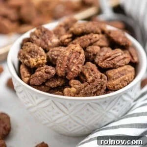 An inviting bowl of perfectly candied pumpkin spiced pecans, featuring autumnal striped linen and a baking pan in the background.