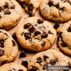 A delightful array of One Bowl Small Batch Chocolate Chip Cookies, fresh from the oven, lined on parchment paper with tempting crumbs and extra chocolate chips scattered around.