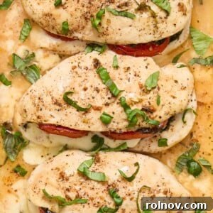 Close-up view of perfectly cooked Mozzarella Stuffed Chicken breasts, generously filled and topped with vibrant, freshly chopped basil and ripe tomatoes for a beautiful Caprese-inspired dinner.