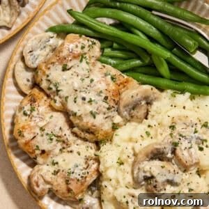 Plate with creamy chicken thighs and mushrooms with mashed potatoes and green beans.