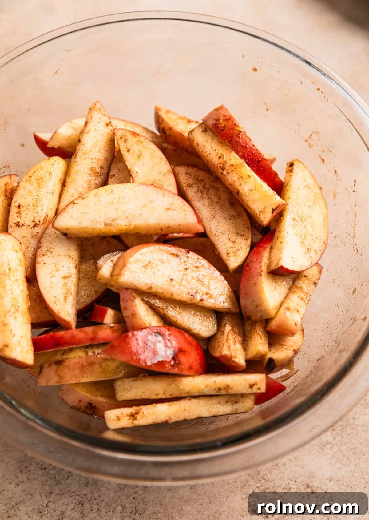 Air Fryer Cinnamon Apple Slices 3 Sliced apples tossed in oil and cinnamon in a glass mixing bowl, ready for the air fryer.