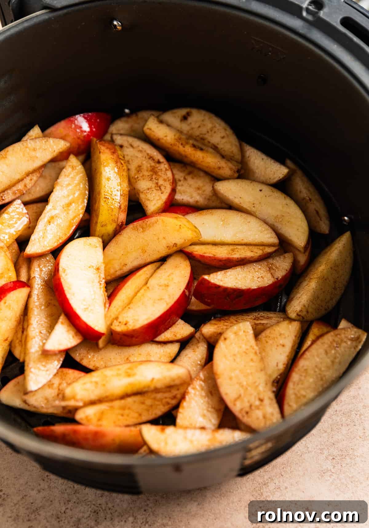 Air Fryer Cinnamon Apple Slices 4 Air fryer basket with a single layer of sliced apples tossed in oil and cinnamon, before cooking.