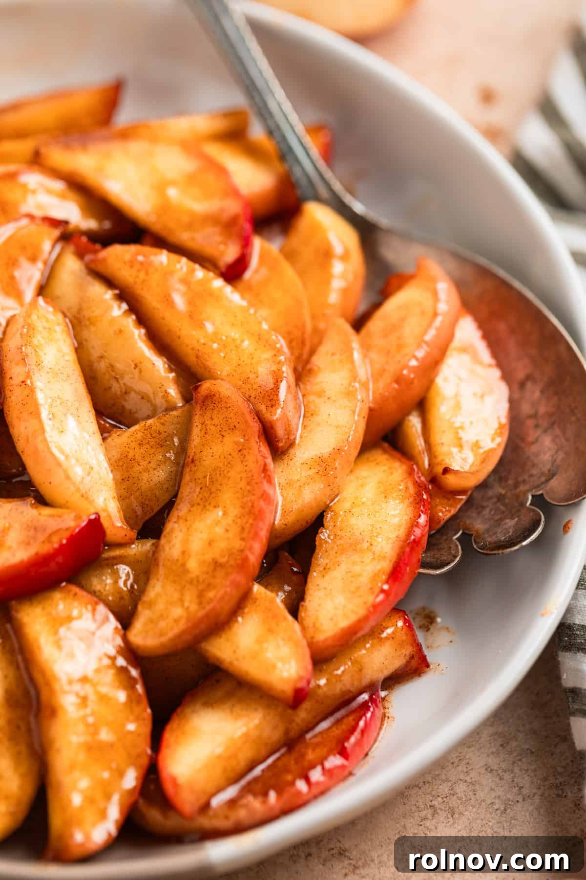 Air Fryer Cinnamon Apple Slices 8 Air fried apples arranged attractively on a white serving dish with a spoon, highlighting their tender texture and golden color.